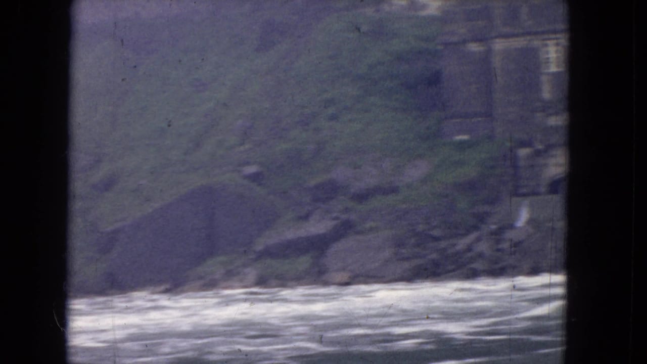 1964 8mm river view near Niagara Falls, with rushing water, a dark window divider and a soft green hillside partly obscured by film softness.