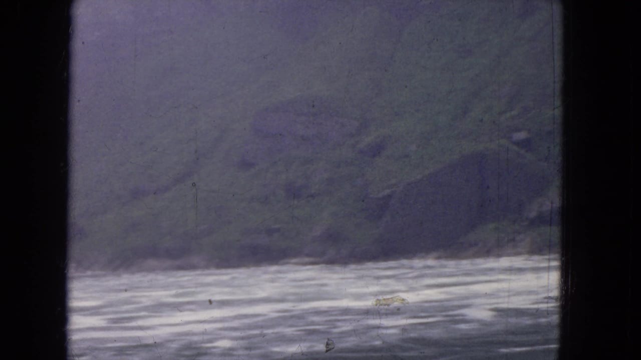 1964 8mm frame near Niagara Falls showing moving river water and a muted green rocky riverbank, divided by dark window framing.