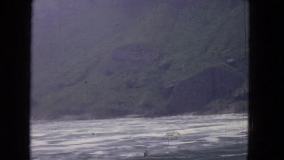1964 8mm frame near Niagara Falls showing moving river water and a muted green rocky riverbank, divided by dark window framing.