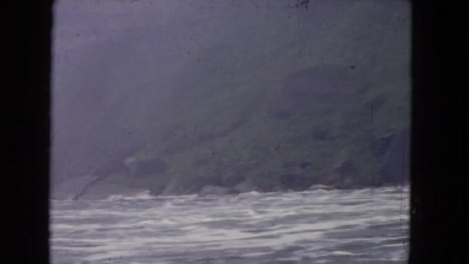 1964 8mm travel footage showing rippling water and a misty distant shoreline through a dark window opening.