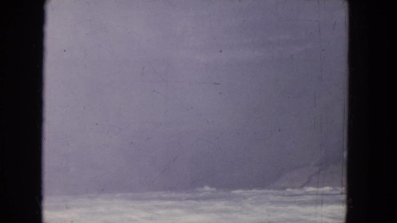 Soft, faded 8mm frame with pale moving water and haze seen from behind a window during a travel sequence.