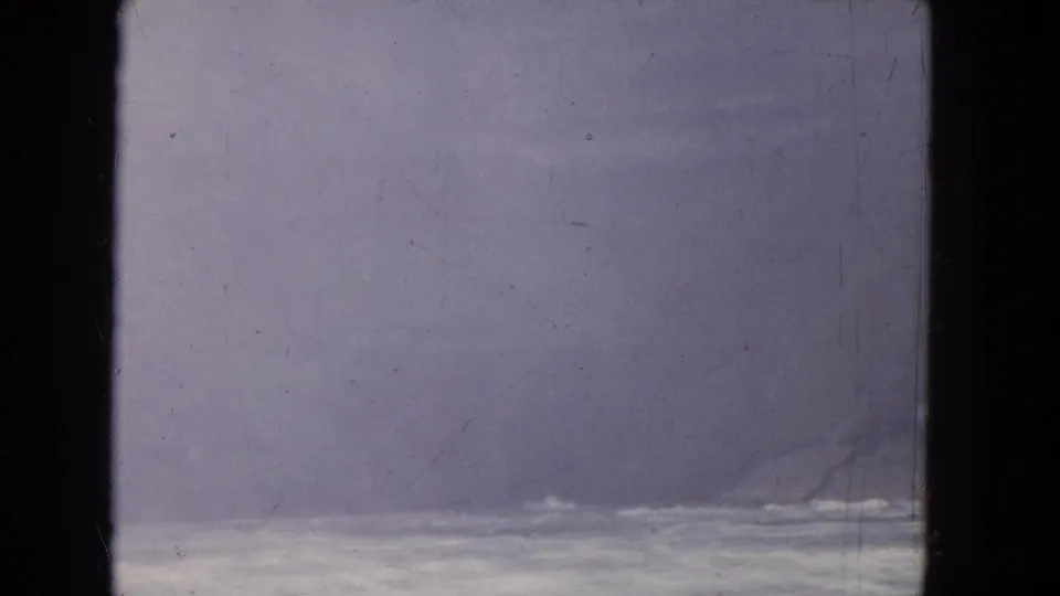Soft, faded 8mm frame with pale moving water and haze seen from behind a window during a travel sequence.