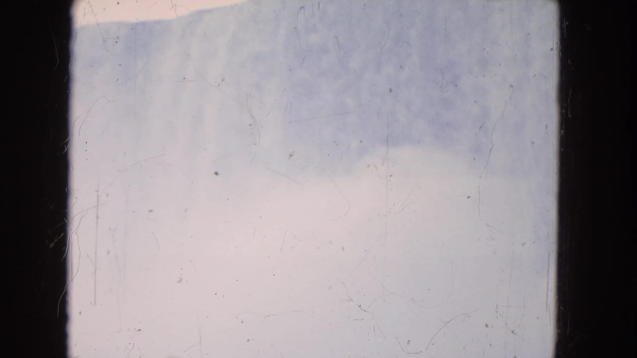 1964 8mm home-movie frame, likely Niagara Falls area, showing pale sky and a low water band with visible film scratches.