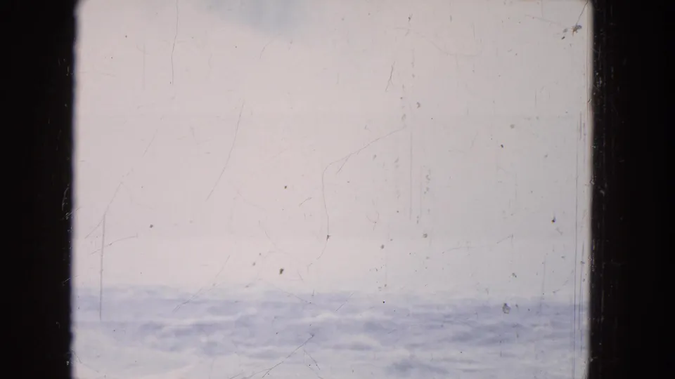 1964 8mm travel-film frame showing a rippled water band beneath pale sky, with scratches and slight exposure variation.