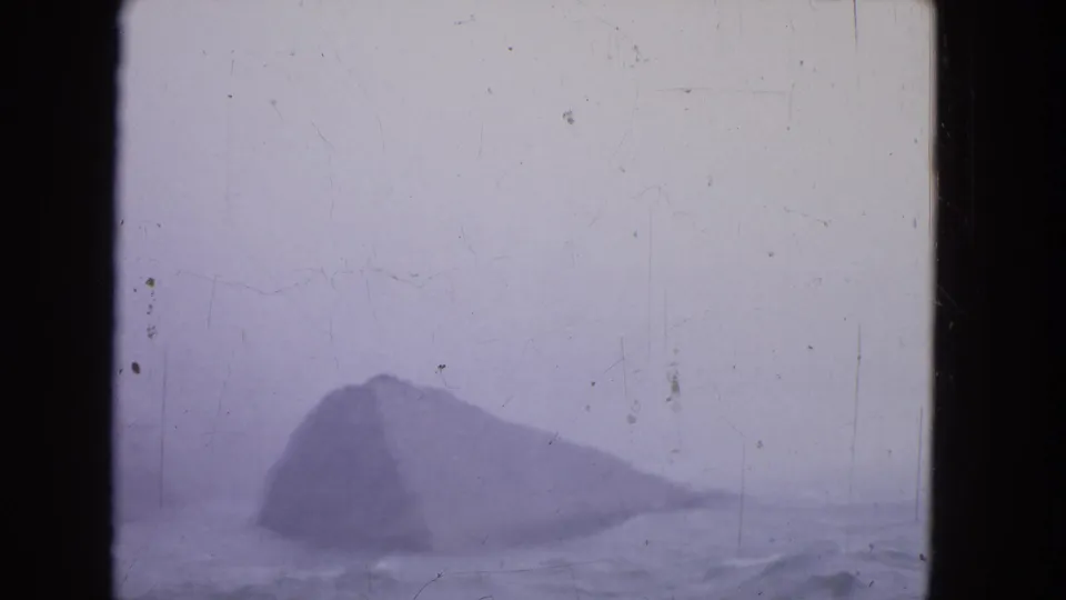 A hazy 1964 Niagara Falls view shows a dark rock form in mist, soft water movement, purple tint, and scratched 8mm texture.
