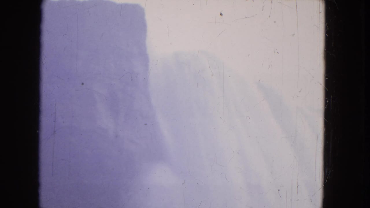 1964 Niagara Falls 8mm frame showing soft pale water, blue-purple mist, dark film edge, dust, and scratches.