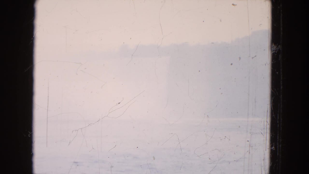 Mist-softened waterfall and shoreline seen across water within the film gate.