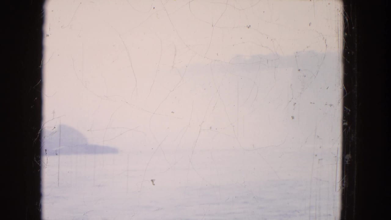 Hazy 1964 8mm view from Niagara Falls, with calm water in the foreground and a dark cliff or shoreline shape at left.