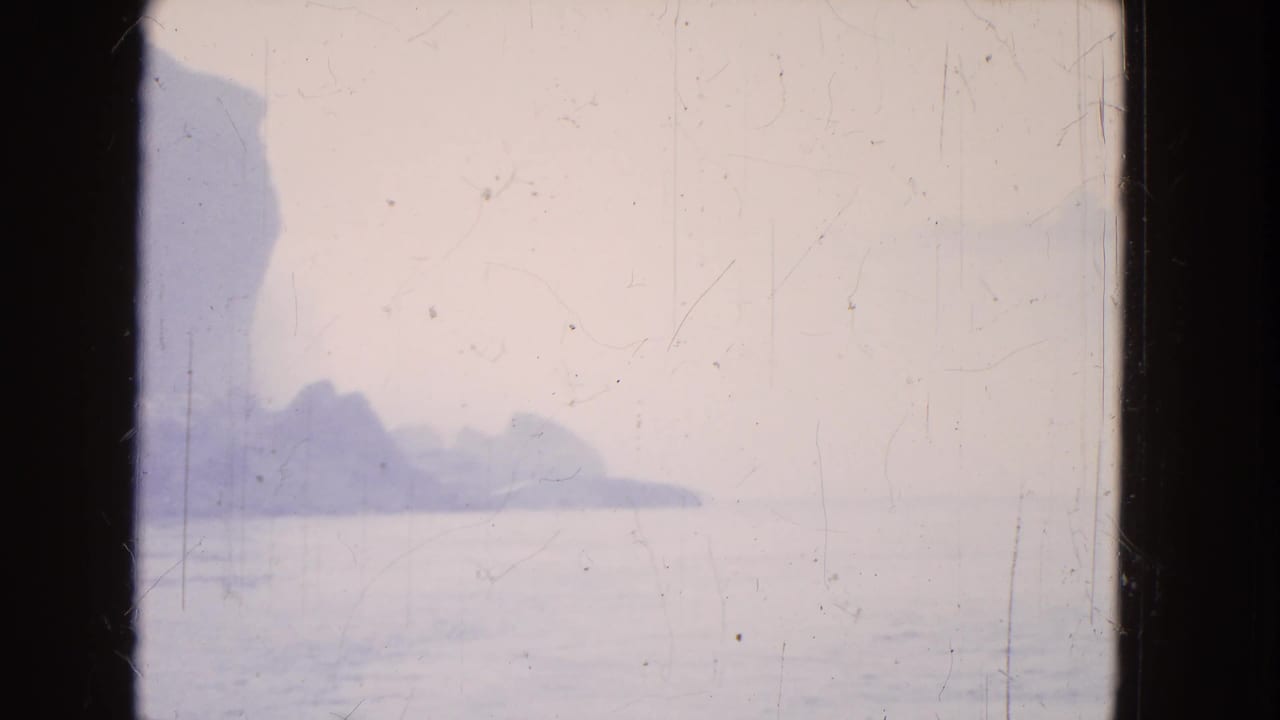 Niagara Falls appears through haze in a 1964 8mm frame, with a darker cliff silhouette and calm water below.