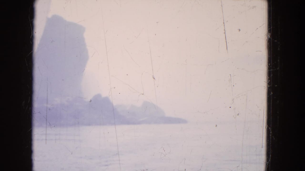Distant rocky cliffs and pale water seen through a dark window frame.