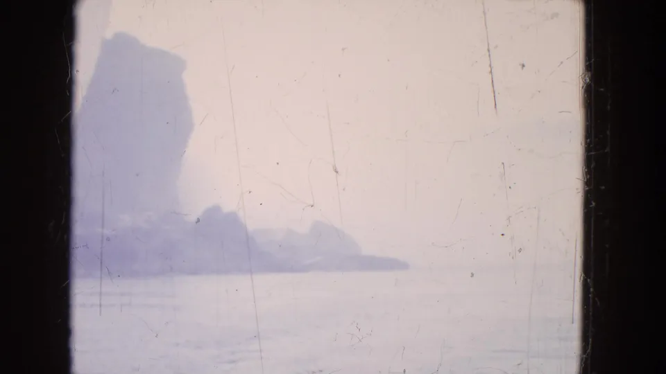 1964 8mm travel frame showing distant cliffs, haze, and water at Niagara Falls through a dark boat window or porthole.