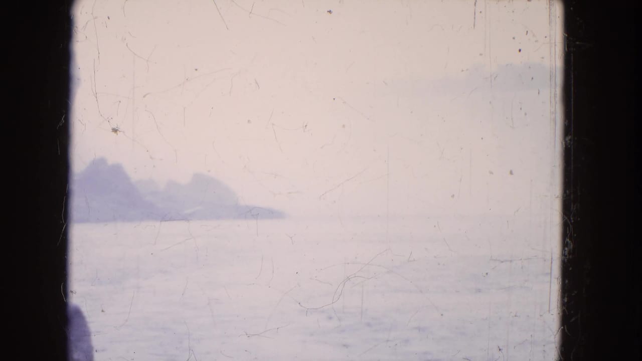 Soft 8mm view of a rocky Niagara Falls shoreline and water, partially obscured by dark boat-window framing.