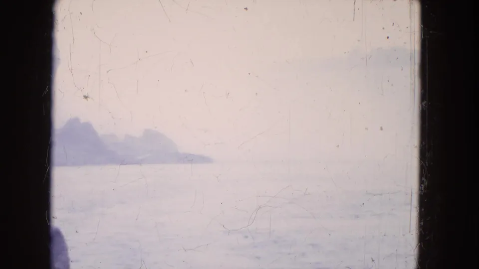 Soft 8mm view of a rocky Niagara Falls shoreline and water, partially obscured by dark boat-window framing.