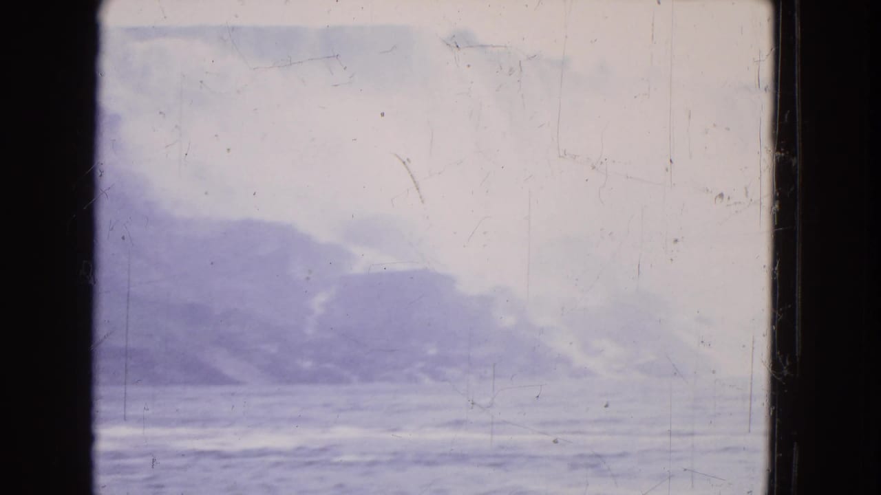 Boat-level 1964 home-movie frame of turbulent water and mist near a rocky cliff at Niagara Falls.