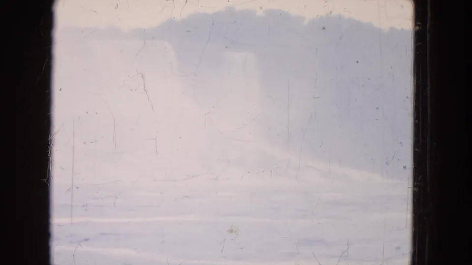 1964 8mm home-movie frame with a hazy landform, pale sky, and softly rippled water across the lower view.