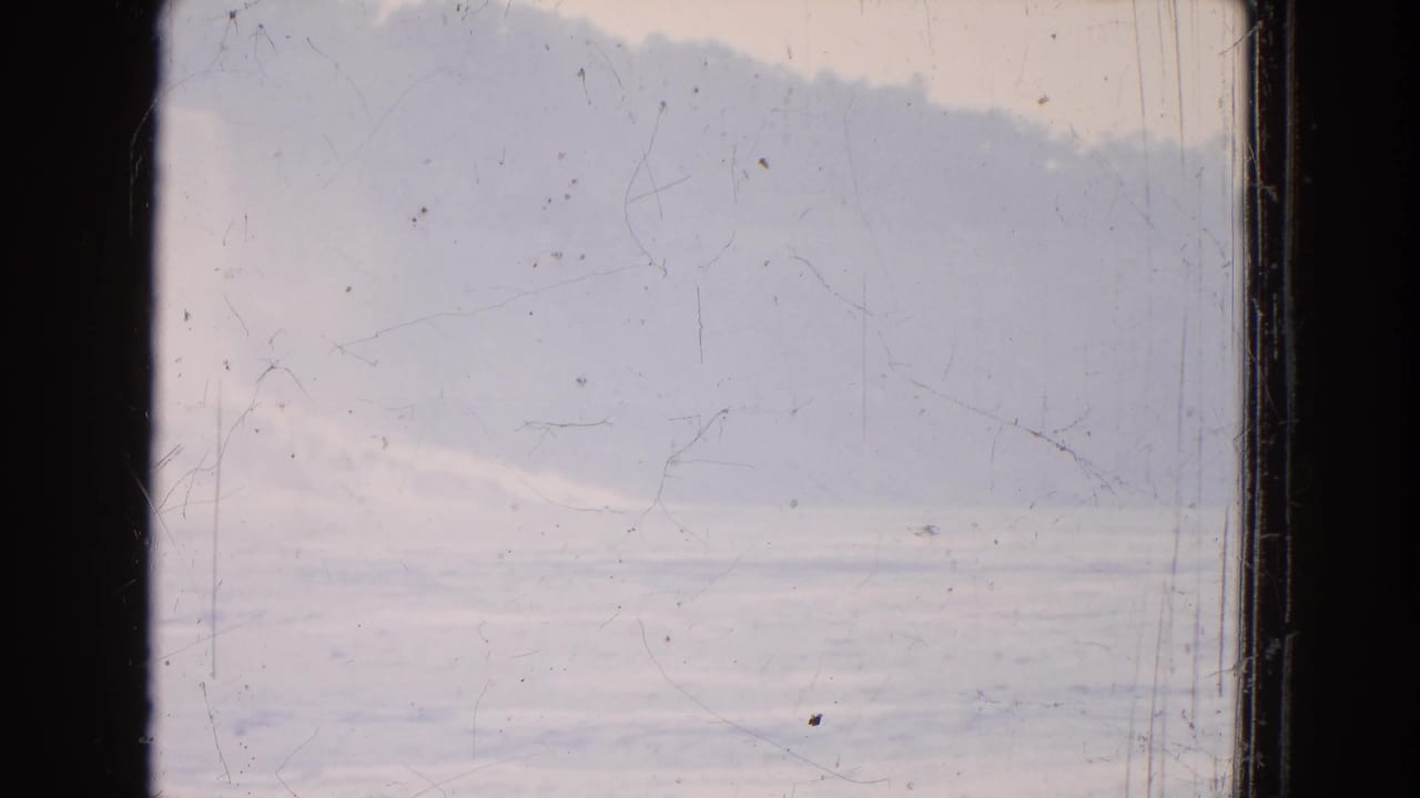 1964 8mm frame showing hazy water, a soft cloud bank or landform, and visible scratches on the film surface.