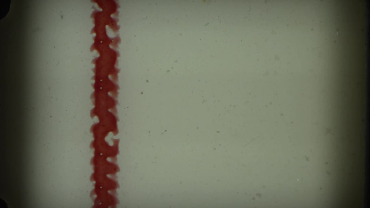 Vertical red painted line on a pale background with dark film borders.