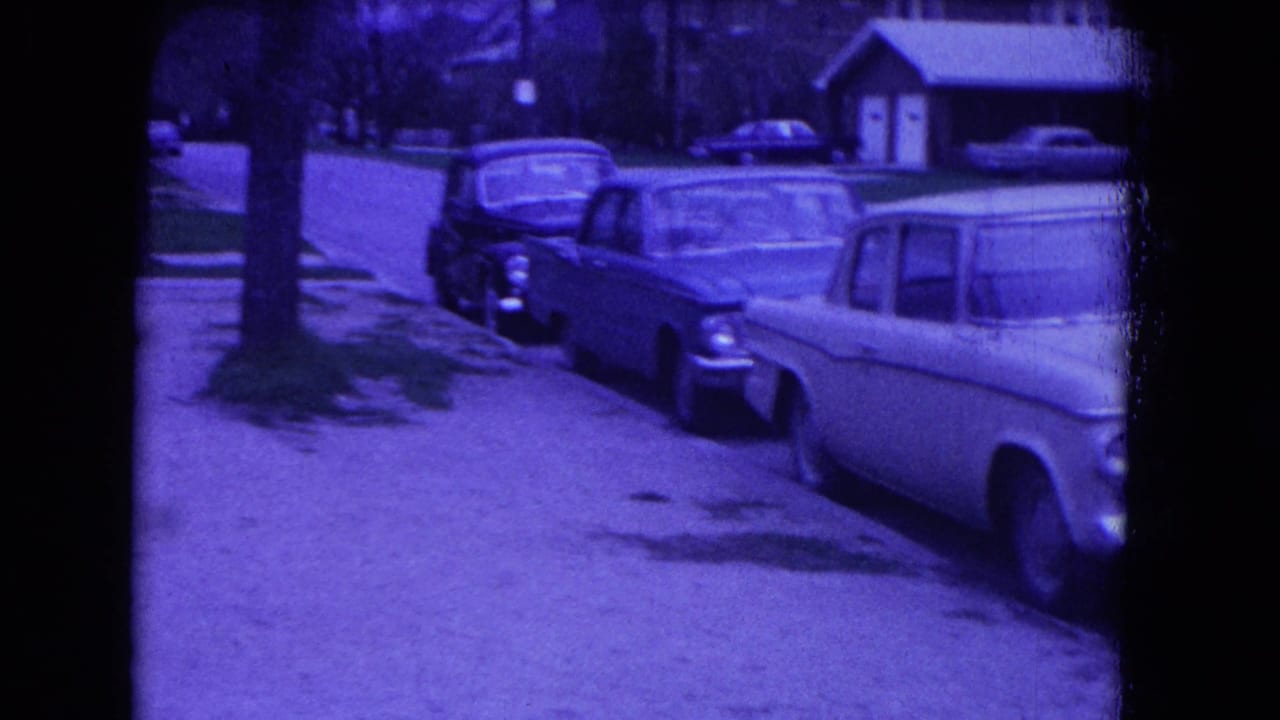 Parked vintage cars along a quiet residential street with houses and bare trees.