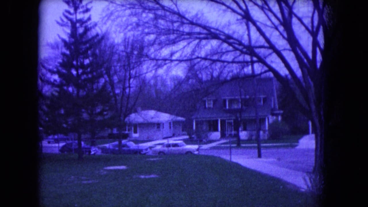 1964 Niagara Falls home-movie view across a suburban lawn toward houses, bare trees, and parked cars on the opposite side of the street.