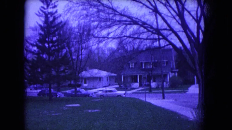 1964 Niagara Falls home-movie view across a suburban lawn toward houses, bare trees, and parked cars on the opposite side of the street.