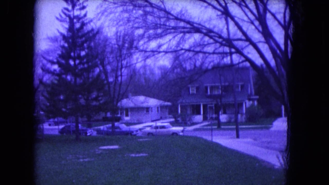 Similar view of houses, bare trees, lawn, sidewalk, and parked cars on a quiet street.