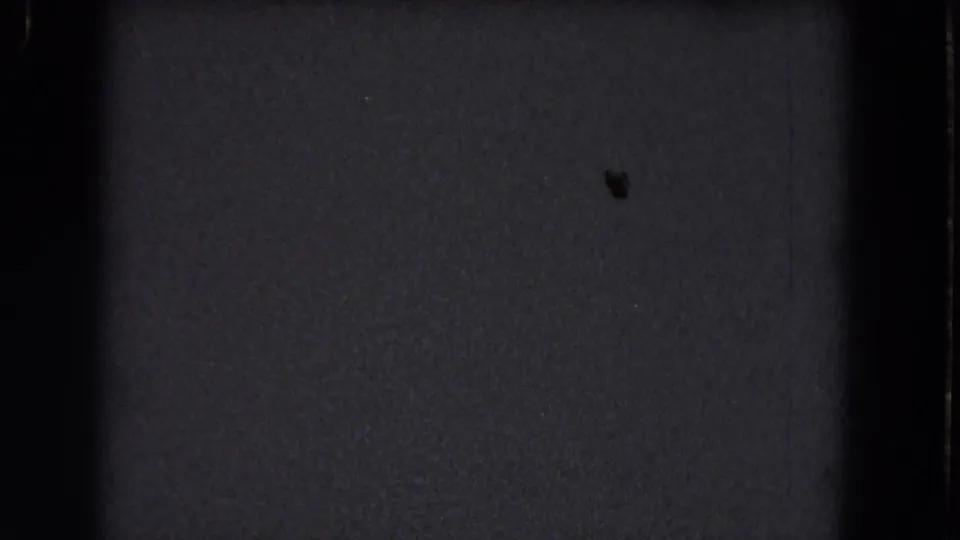 Dark 1964 8mm home-movie frame from the Niagara Falls reel showing grain, gate shadow, and a tiny dust mark.
