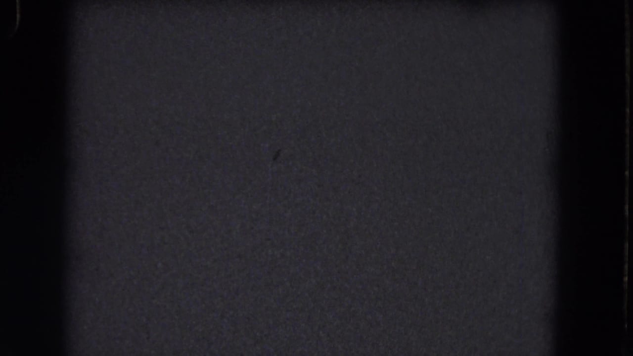 Dark 1964 8mm home-movie frame with visible grain, dust specks, and soft vertical gate borders; no subject is visible.
