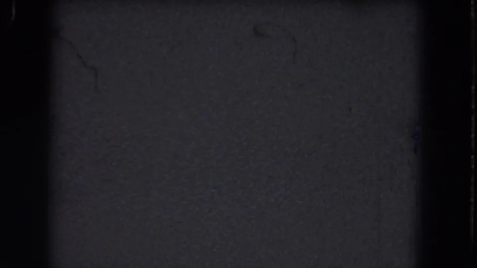 Dark 1964 8mm reel frame from the Niagara Falls metadata set, showing grain, frame edge shadows, and tiny dust specks.