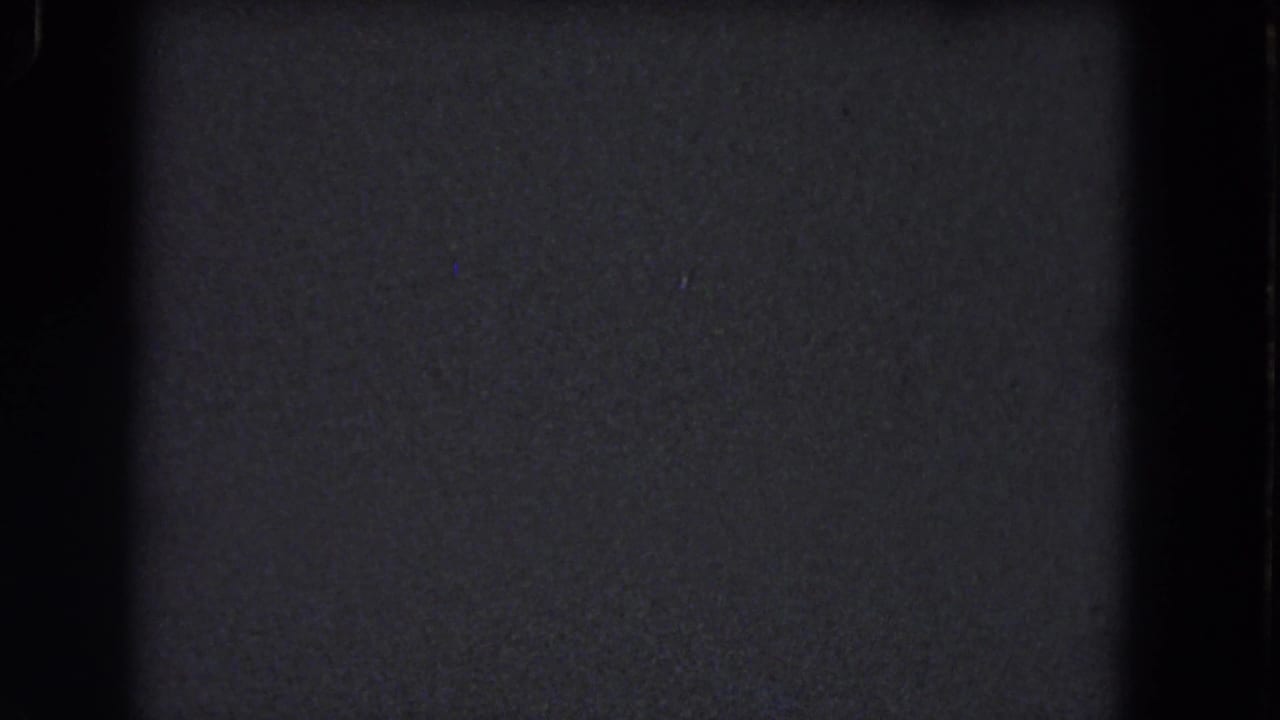 A dark 8mm frame from the 1964 Niagara Falls reel, dominated by grain, vertical gate shadow, and faint dust particles.