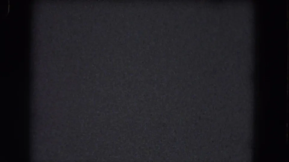 Dark Niagara Falls reel frame from 1964 showing 8mm grain, vertical frame-edge shadow, and small blue-white dust marks.