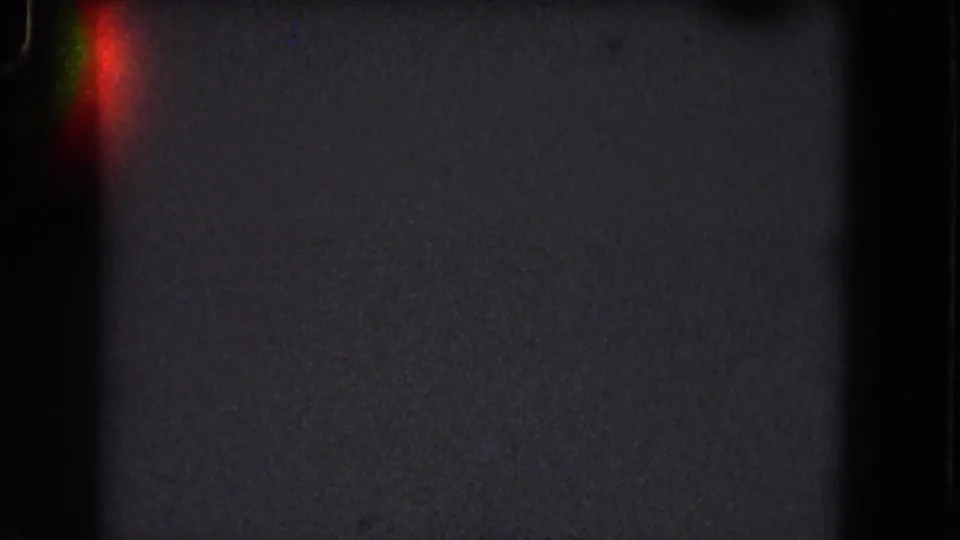 Dark 8mm frame with a red-green light flare at the left edge, grain across the field, and no identifiable location detail.
