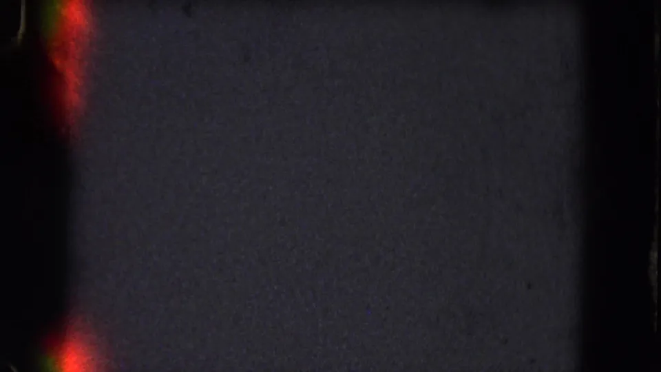 Low-light 8mm frame showing red flares near the left edge and lower frame, with visible grain and dark film borders.