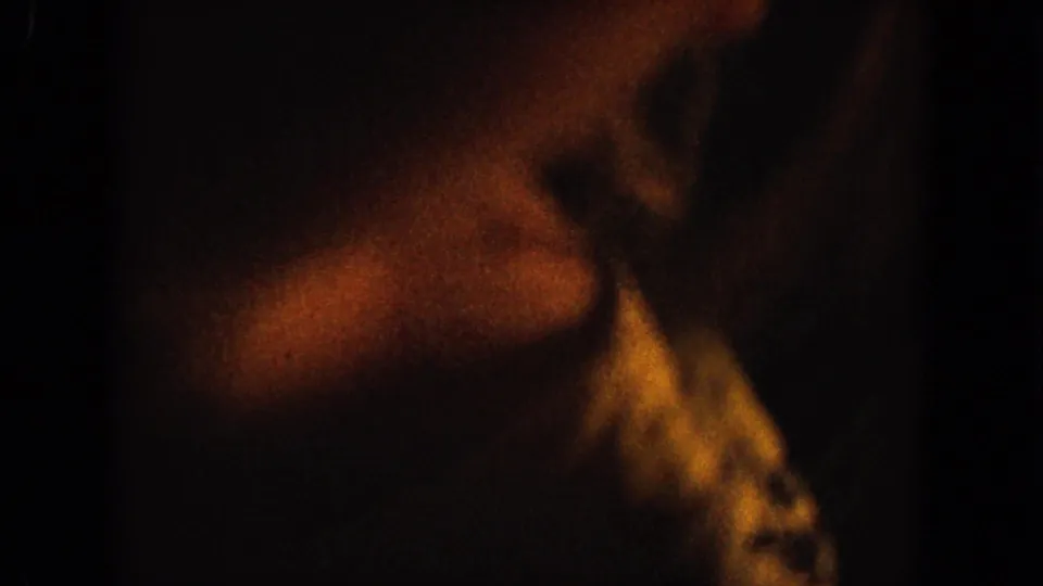 Soft, blurred 8mm close-up of a hand or arm moving through dim warm interior light, likely during the gesture sequence.