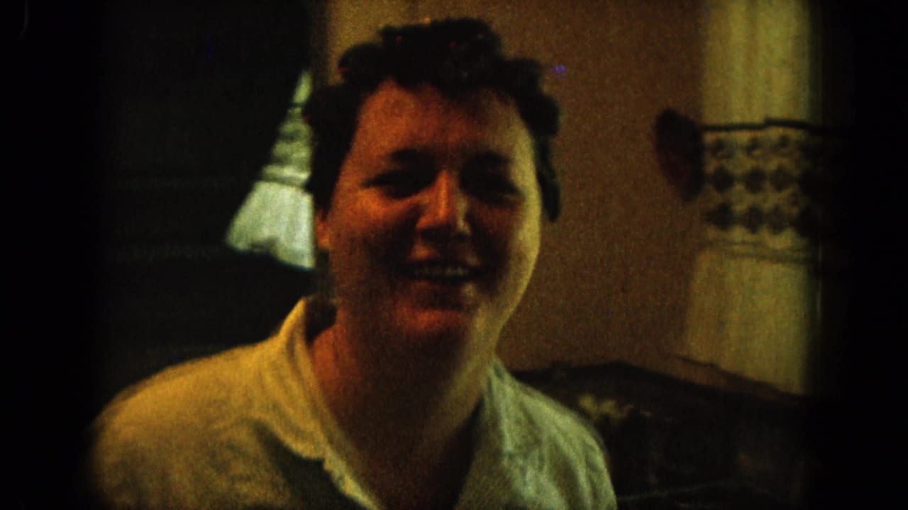 Smiling woman with short dark hair seated indoors in dim warm light.