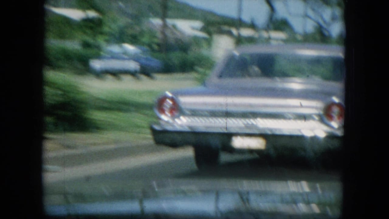 A silver mid-1960s sedan drives ahead on an Oahu coastal road, viewed from inside another moving vehicle.