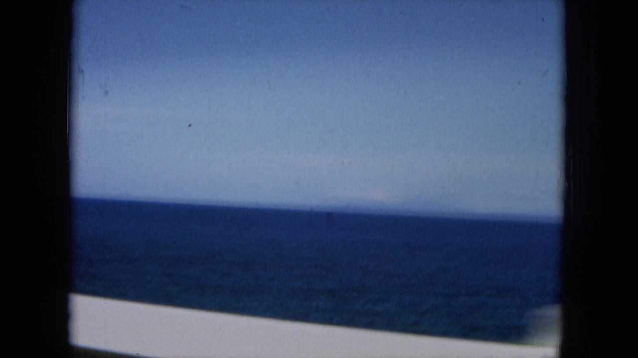 Blue ocean horizon seen from a moving vehicle with dark film frame edges.