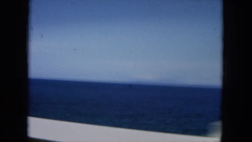 1964 Hawaii 8mm frame showing a blue ocean horizon from a moving car, with dark gate edges and soft motion blur.