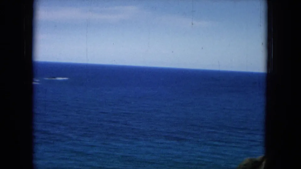 1964 8mm frame showing an open Hawaiian ocean horizon with dark film borders and a small foreground rock edge.