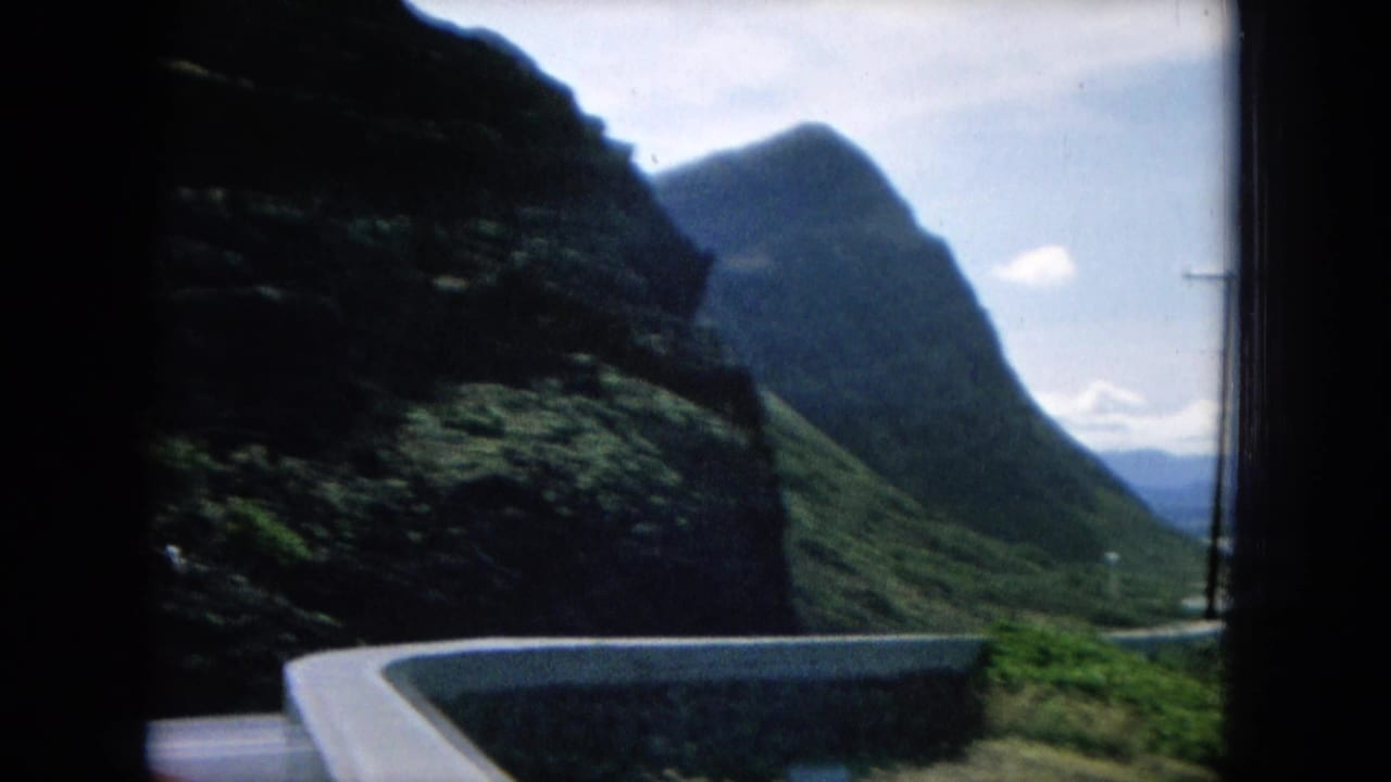 Curving road beside steep green mountains with distant sky and valley.