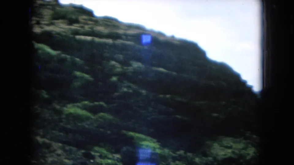 Soft 8mm frame of a rugged green hillside in Hawaii, filmed from a moving travel viewpoint.