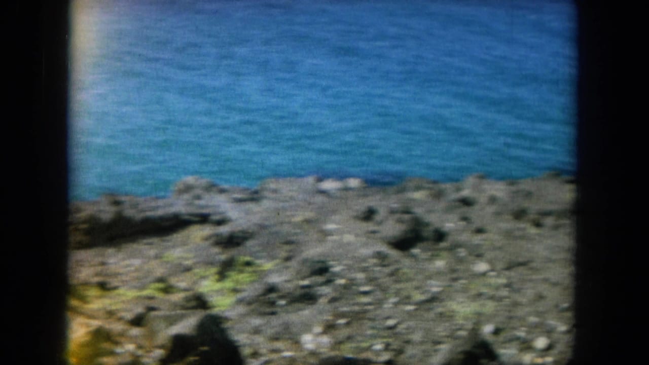Rocky shoreline with blue ocean beyond, seen through dark 8mm frame edges.