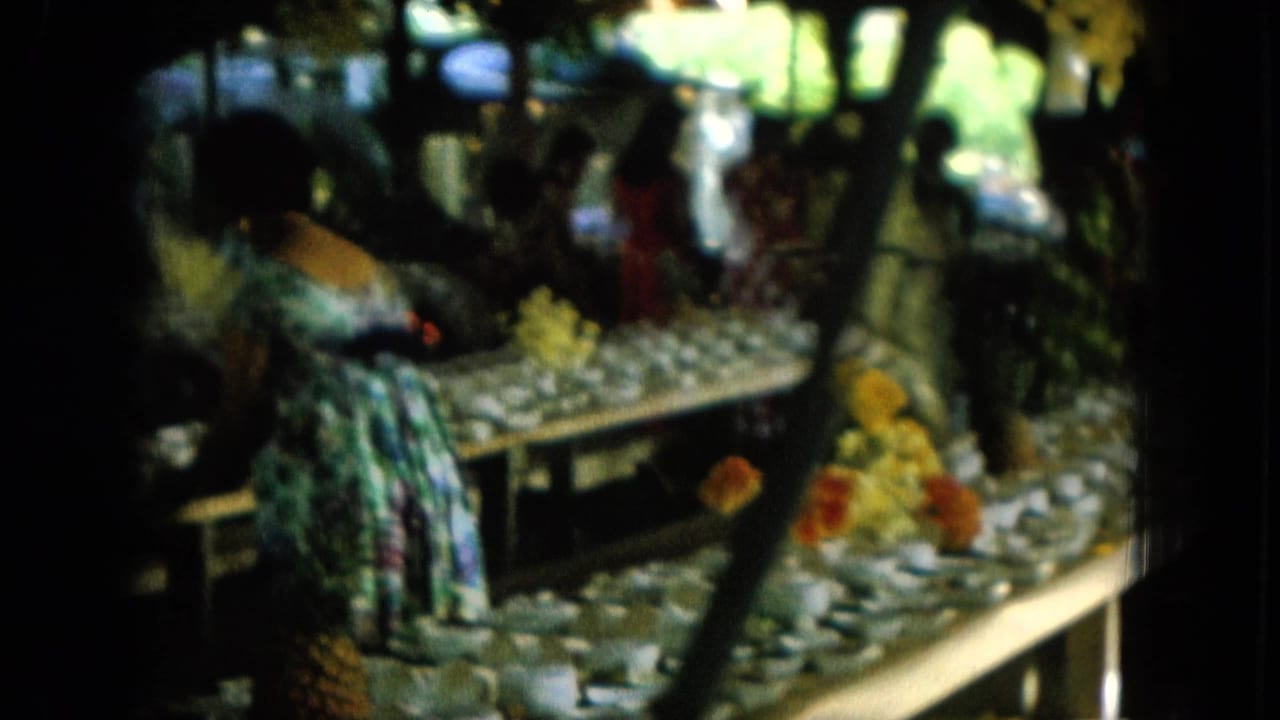 Women near long tables covered with small bowls in a shaded outdoor fair setting.