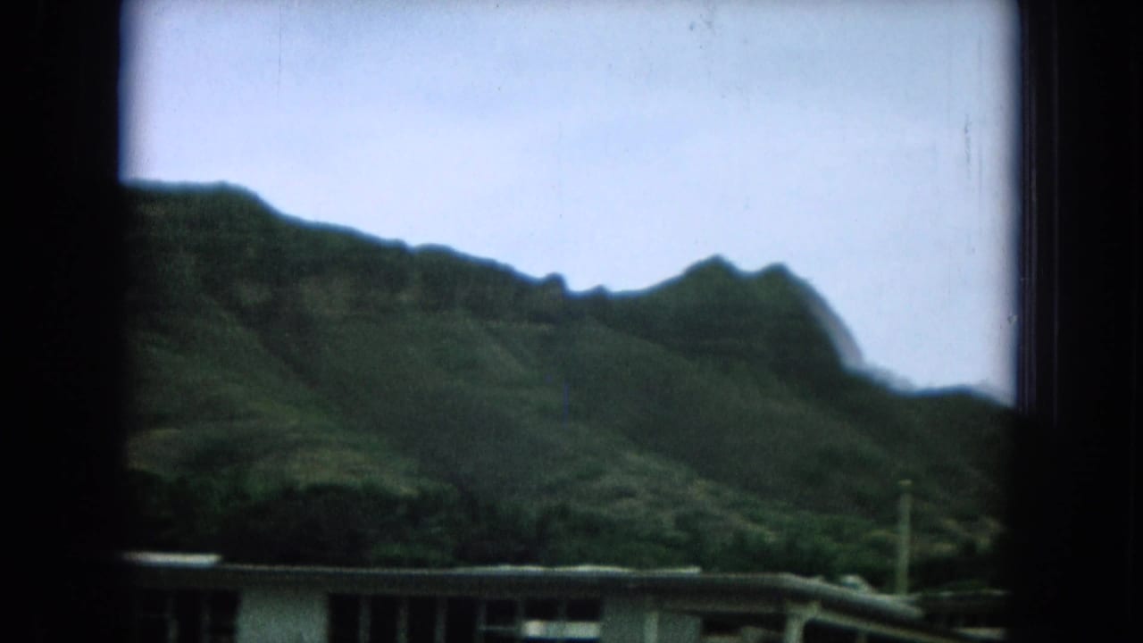 Green hillside and rooftops partly obscured by a dark vertical window frame.