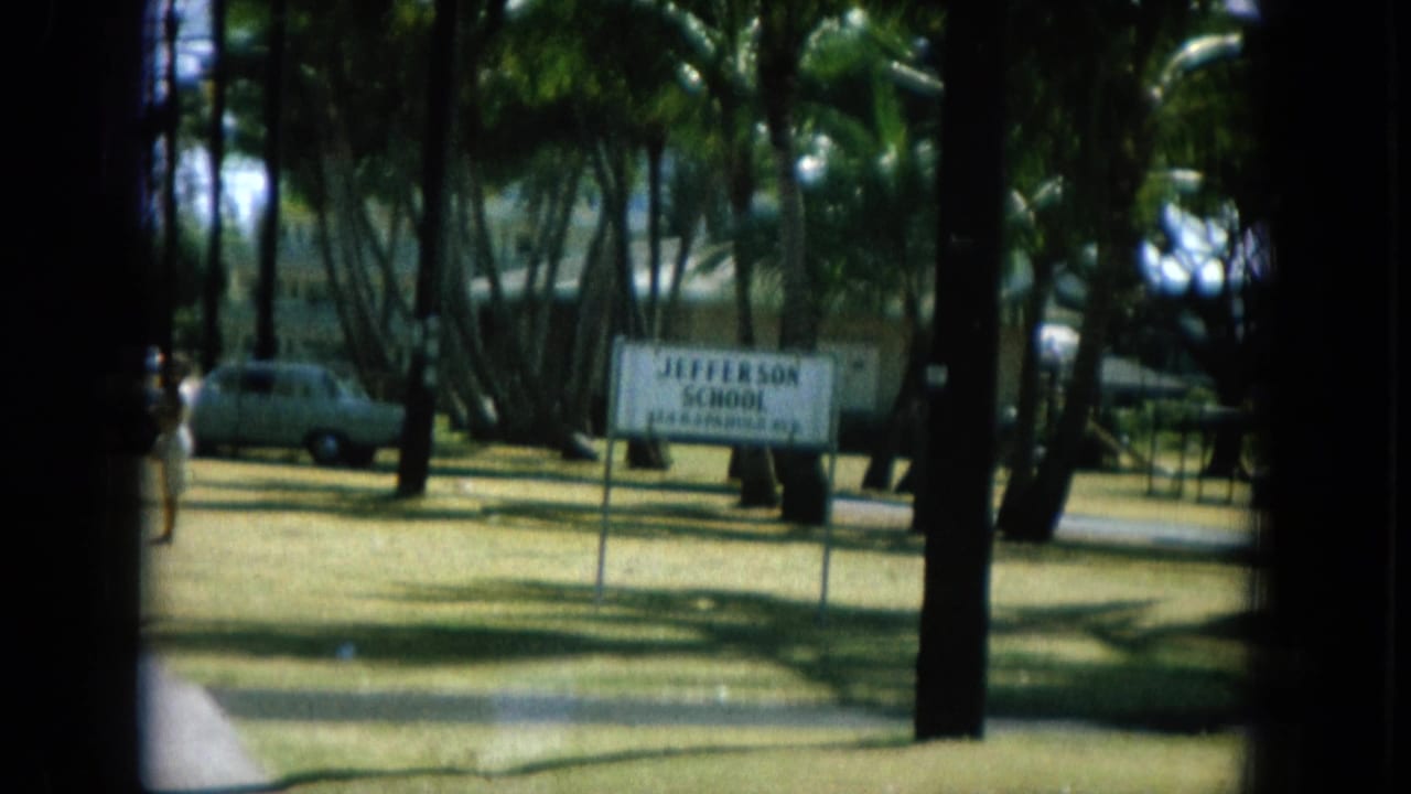 Jefferson School sign beside palms and a parked car on a sunny lawn.
