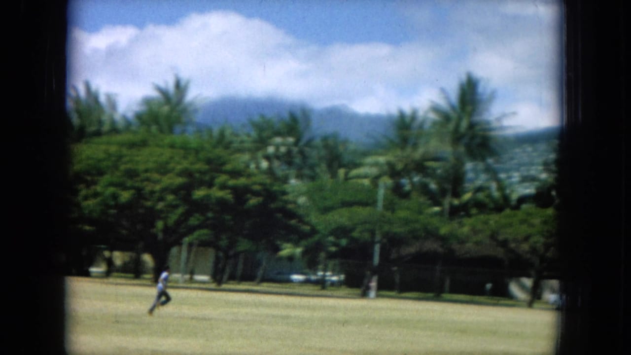 Runner crossing the field with palms, mountains, and scattered clouds behind.