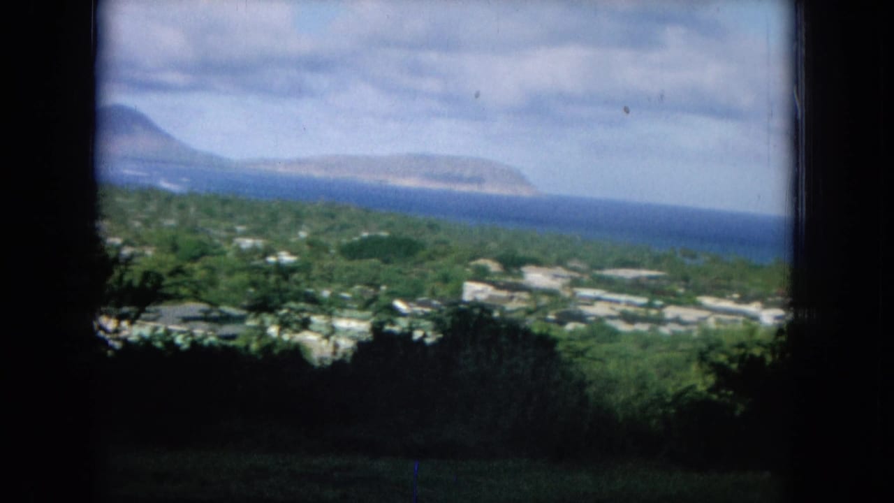 Elevated view of green hills, scattered buildings, blue ocean, and distant land through a dark frame edge.