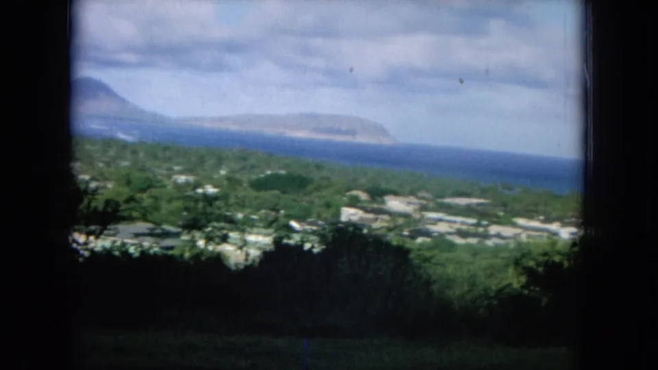 1964 8mm Oahu footage appears to show green coastal hills, low buildings, ocean water, and distant land under a cloudy sky.