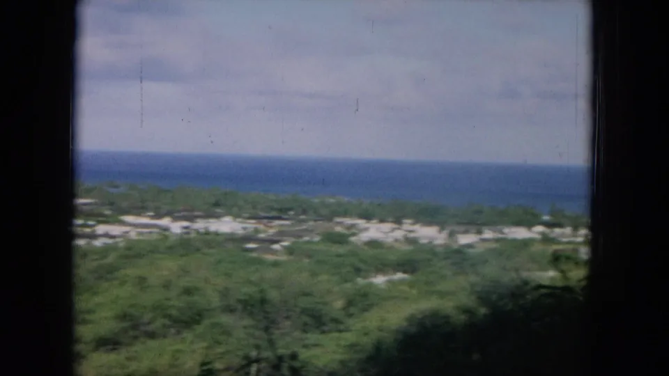 1964 Oahu footage appears to show a broad ocean horizon beyond green coastal land and low residential structures.