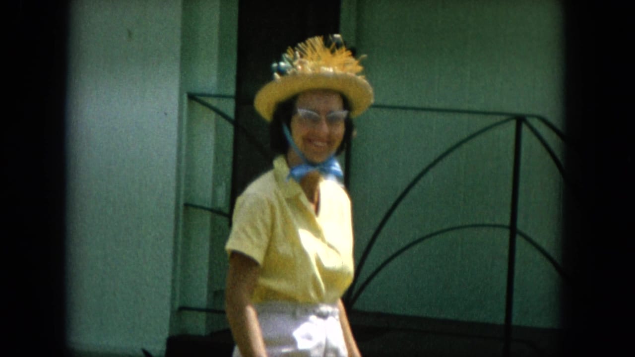 A smiling woman in 1960s-style yellow clothing and straw hat faces the camera outside in Oahi, Hawaii, according to clip metadata.