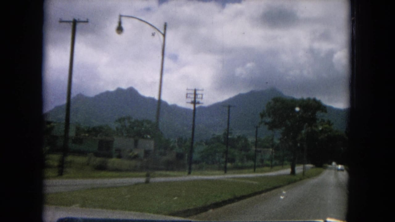 Roadside view with utility poles, grassy verge, cloudy sky, and mountain ridge.